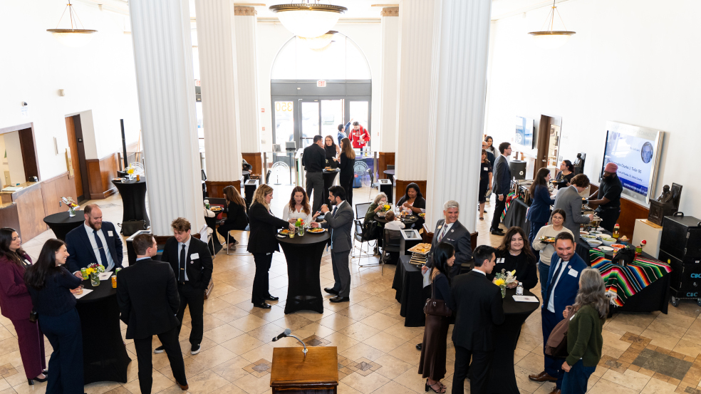 Groups of people stand around waist high tables throughout a large room hosting the ceremony celebration