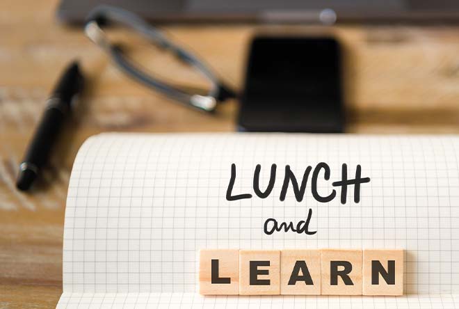 Lunch and learn words in front of notebook on desk with pens and computer