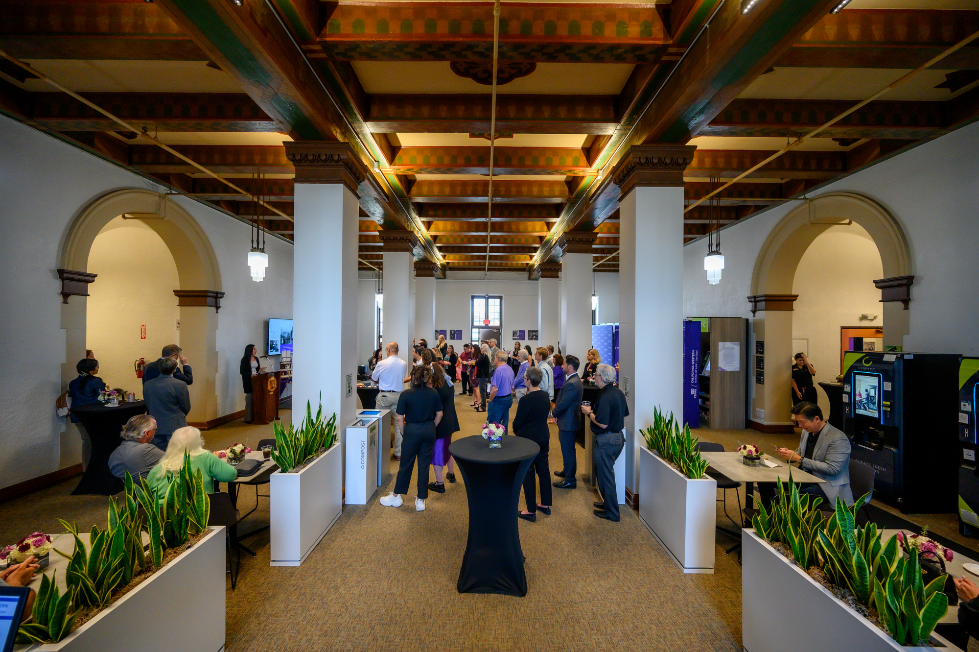 A crowd gathers in a lobby with high painted ceilings and arched entryways.