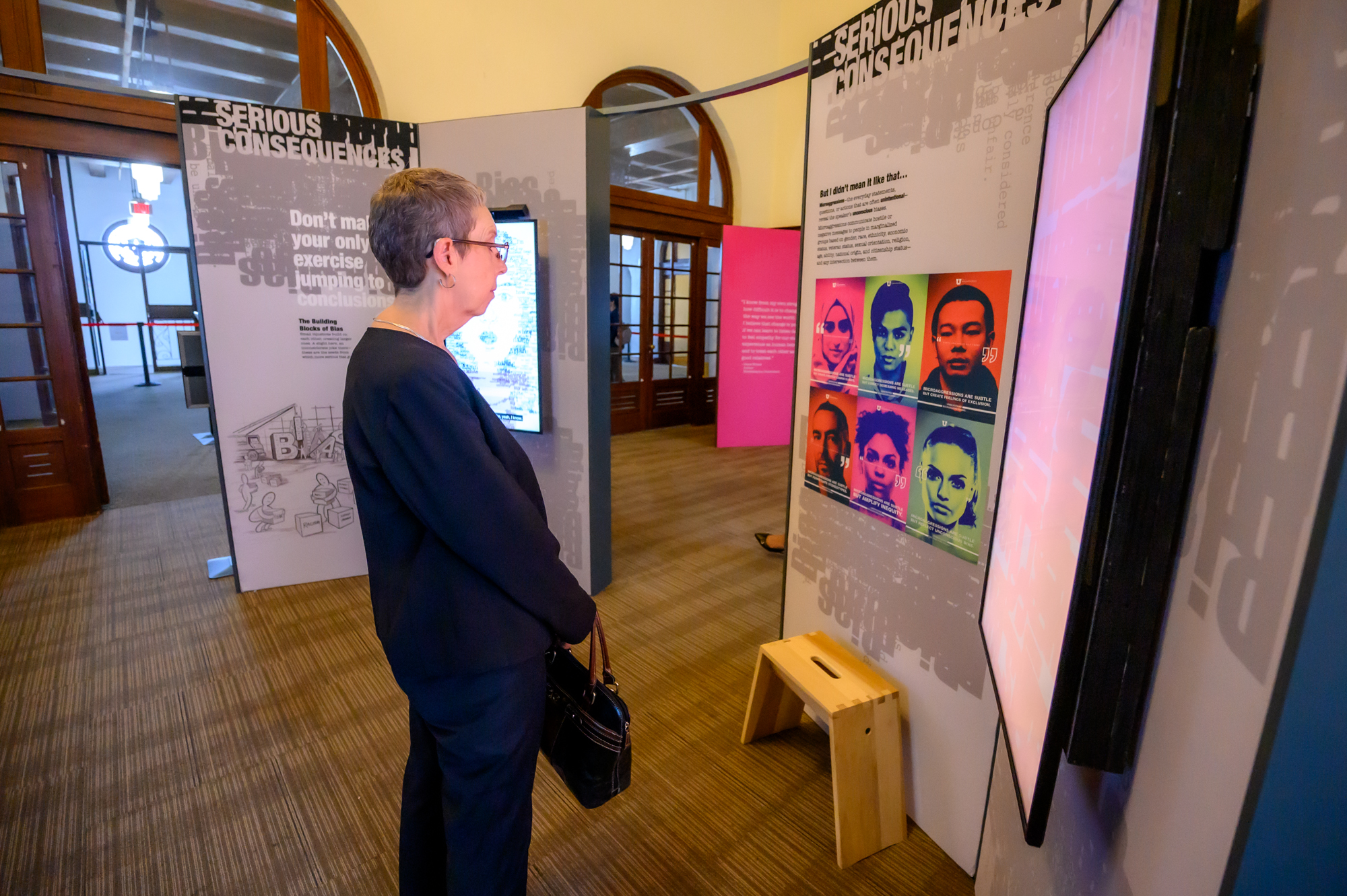 A woman in all black stands in an exhibit watching a demo on a screen.