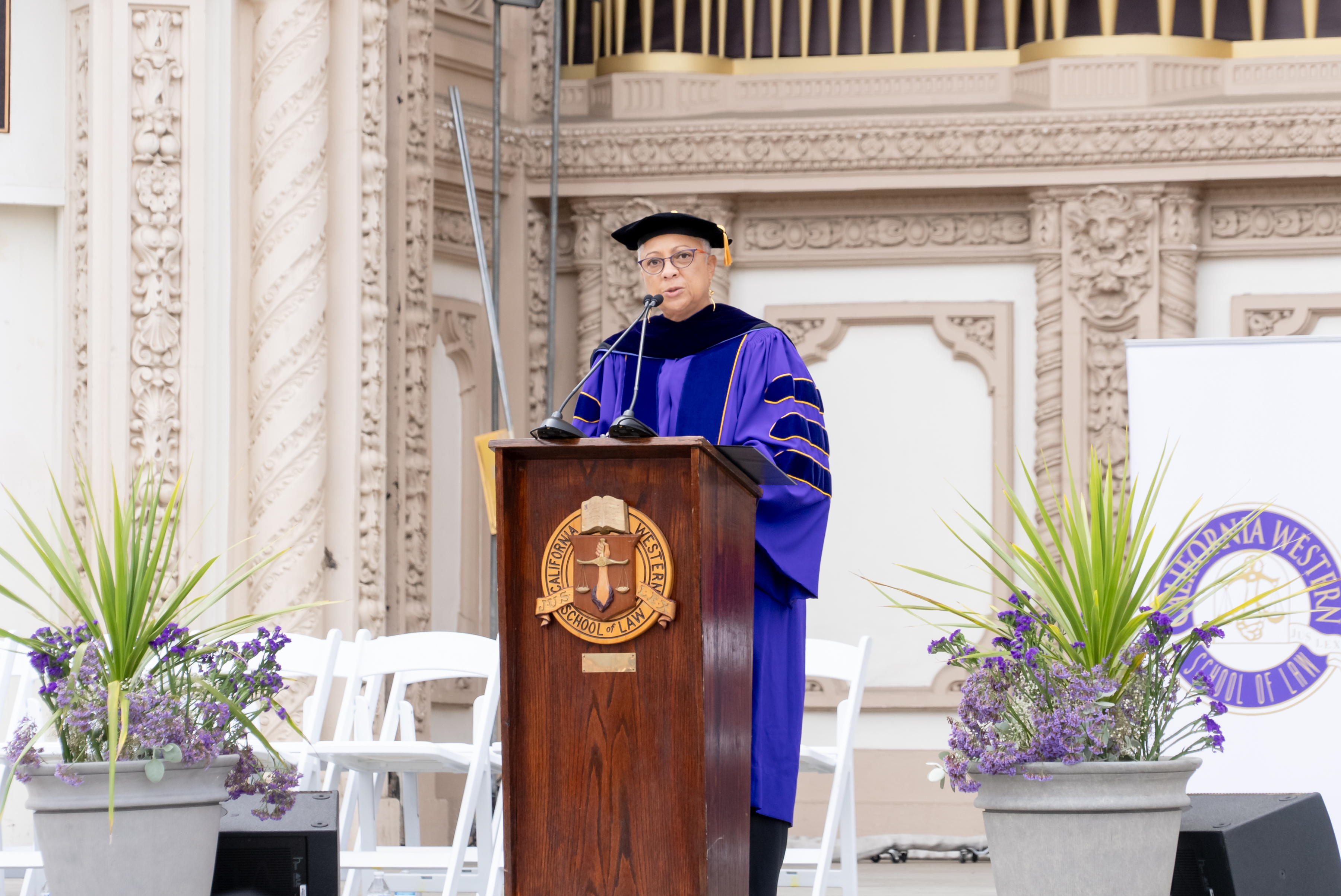 Dean Scott stands behind a wooden podium with the California Western School of Law seal wearing purple and black commencement regalia.