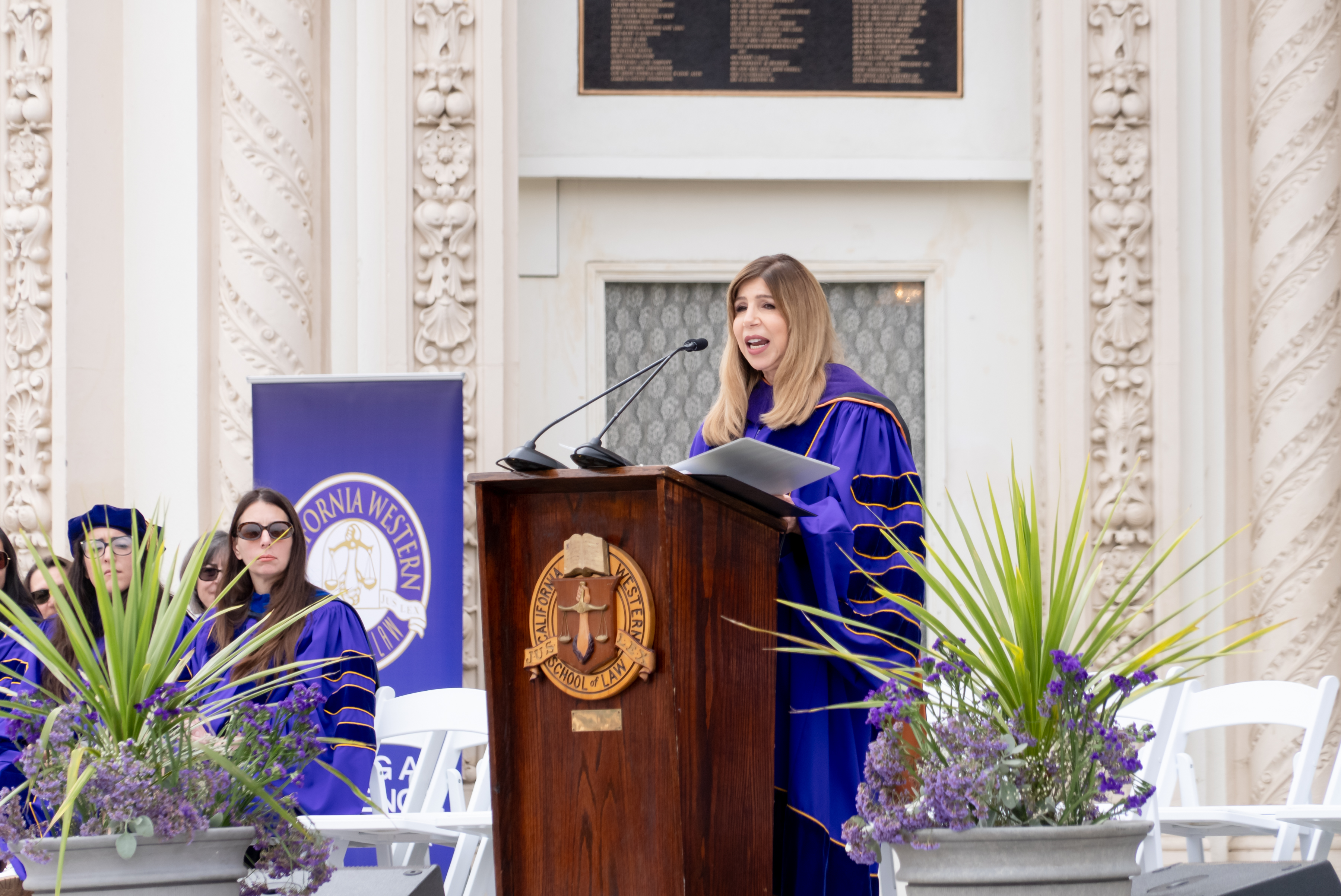 Summer Stephan stands behind a wooden podium with the CWSL seal on it wearing purple commencement regalia.