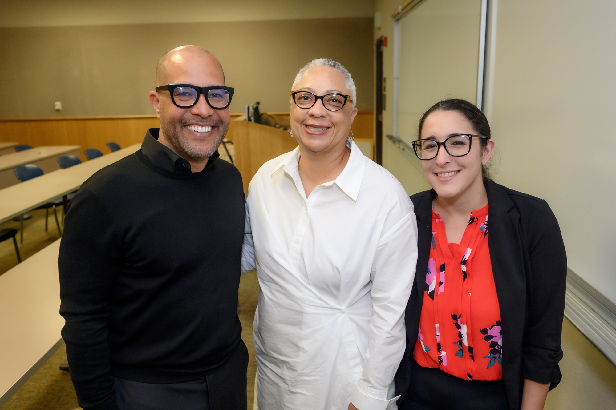 George Fatheree - in a black collared shirt, Dean Sean Scott - in a white collared dress, and Emily Behzadi Cárdenas - in a coral floral shirt and black cardigan, post for a photo.