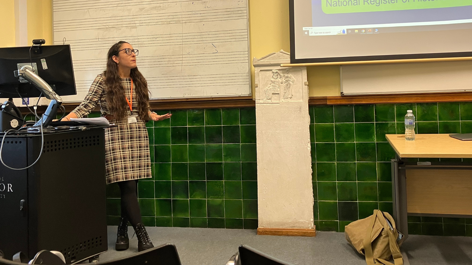 Professor Emily Behzadi Cárdenas stands at the front of a classroom giving a presentation.