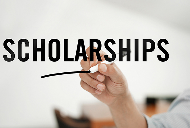 person writing the word scholarship on a glass board